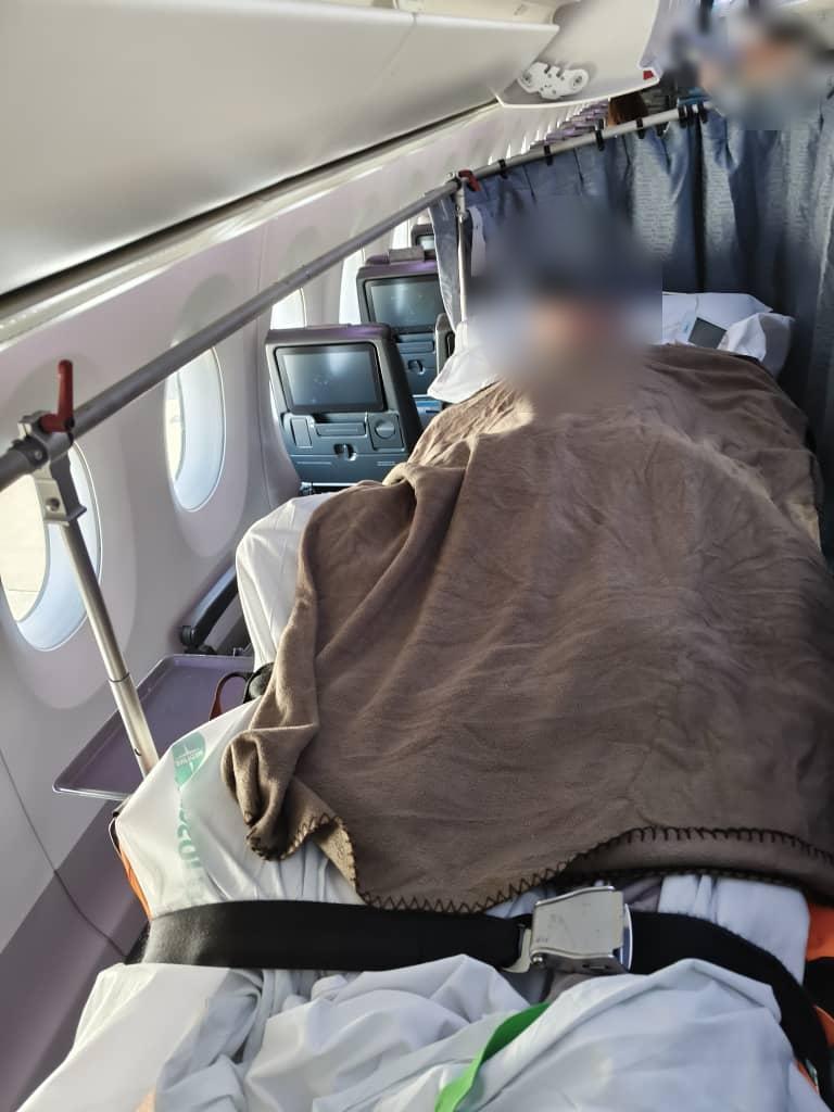 Patient on commercial stretcher inside the aircraft cabin (face blurred for privacy)